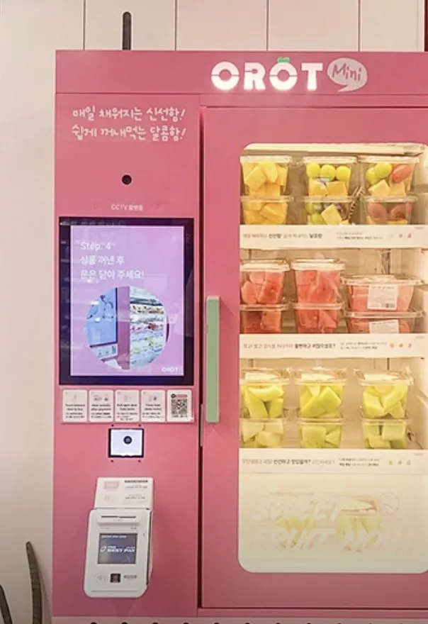 OROT mini kiosk: pink cabinet with touchscreen, card terminal and a lit glass door full of cut fruit cups